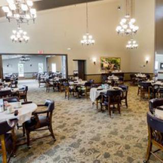 An elegant dining room with multiple tables and chairs, illuminated by chandeliers.