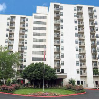A high-rise residential apartment building with multiple balconies, surrounded by greenery.