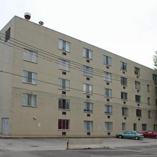 A multi-story apartment building with several windows and parked cars in front.