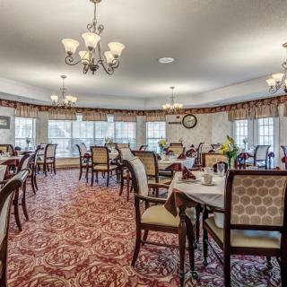 A spacious and elegantly furnished dining room with multiple tables and chairs, decorated with chandeliers and red carpet.