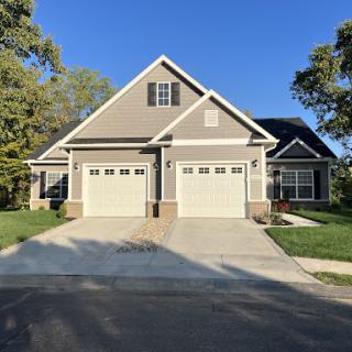A beautiful residential house with a two-car garage and well-maintained landscaping under a clear blue sky.