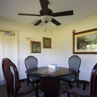 A cozy dining room with a round table, four chairs, and wall artwork under a ceiling fan.