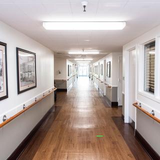 A long, well-lit hospital corridor with handrails and framed pictures on the walls.