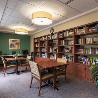 A cozy library reading area with wooden bookshelves, tables, and chairs.
