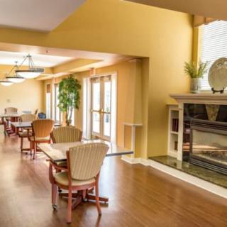 A cozy dining area with tables and chairs, featuring a fireplace and wooden flooring.