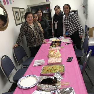 A group of people standing around a table with a variety of food, suggesting a celebration or gathering.