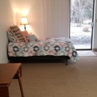 A cozy bedroom featuring a daybed with a colorful quilt, a lamp for lighting, and a window providing an outdoor view.