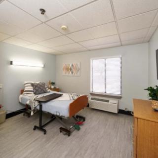 A clean and bright hospital room with a single bed and basic furnishings.