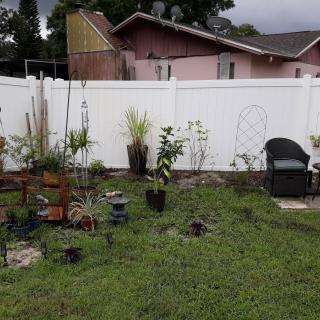 A backyard garden with various plants and a white fence, featuring outdoor seating.