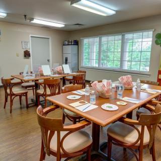 A cozy dining area with neatly arranged tables and chairs, featuring large windows for natural light.
