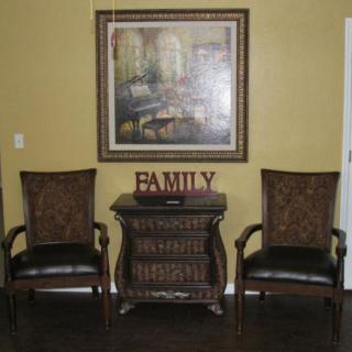 A cozy living room setup featuring two chairs, a central table, and a large painting above.