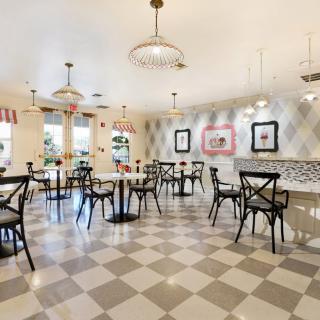 A cozy cafe interior with checkered flooring, stylish lighting, and elegant black chairs surrounding round tables.