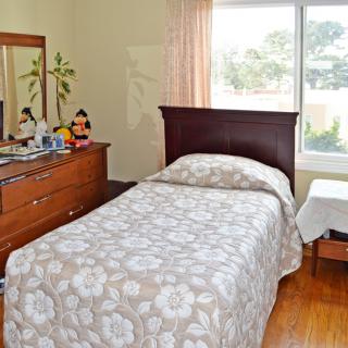 A tidy bedroom with a single bed, dresser, and large window allowing natural light to fill the room.