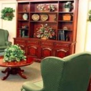 A classic living room setup featuring a wooden bookshelf, green armchairs, and a round coffee table with decorative plants.