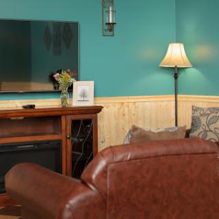 A cozy living room featuring a teal accent wall, modern television, elegant lamp, and comfortable seating.