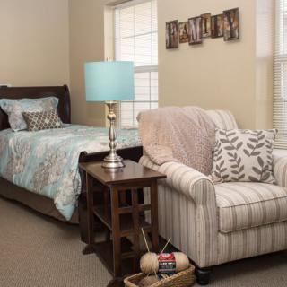 A cozy bedroom with a bed, striped armchair, and a bedside table featuring a lamp.