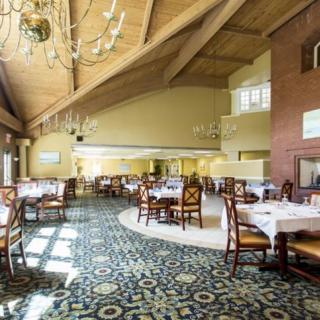 A spacious dining area with elegant chandeliers, neatly arranged tables and chairs, and a patterned carpet.