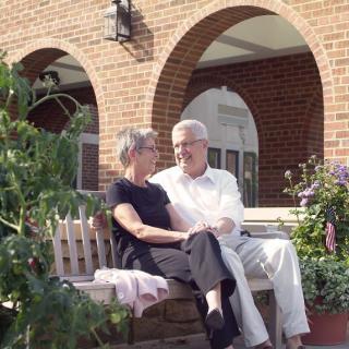 An elderly couple sitting on a bench in a garden, enjoying a conversation.