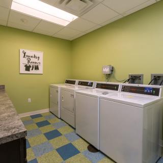 A clean and organized laundry room with washing machines and dryers lined up against a green wall, featuring colorful tile flooring.