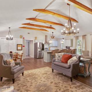 A cozy open-concept living area with vaulted ceilings and wood beams, featuring a kitchen, comfortable seating, and elegant chandeliers.
