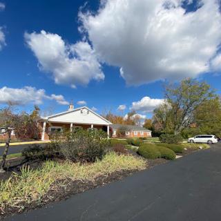 A scenic view of a house surrounded by lush greenery and a clear blue sky with fluffy clouds.
