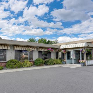 A welcoming entrance to a single-story building under a partly cloudy sky, surrounded by well-maintained landscaping.