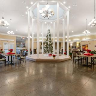 A spacious lobby adorned with a central Christmas tree, surrounded by festive decorations and elegant chandeliers.