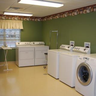 A laundry room featuring multiple washing machines and a dryer against green walls.