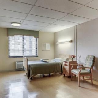 An empty hospital room with a bed, chair, and window.