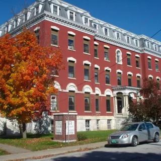 A historic red brick building with autumn trees and a parked car in front.