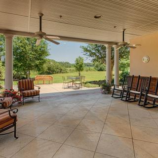 A spacious patio with rocking chairs and ceiling fans, overlooking a scenic landscape.
