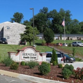 An exterior view of the Hermitage Health Center with a sign, landscaping, and parked cars.