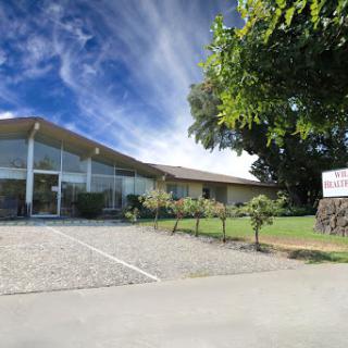 A modern building surrounded by greenery and a clear blue sky.