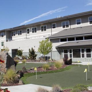 A modern building with a small putting green and landscaped outdoor area under a clear blue sky.
