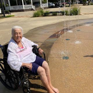 An elderly woman enjoying a sunny day by the fountain, soaking her feet and relaxing.