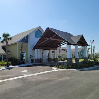 A modern building entrance with a canopy, surrounded by landscaped areas on a clear sunny day.