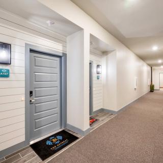 A well-lit apartment hallway with gray doors and a doormat.
