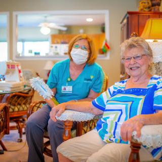 A caregiver smiles alongside an elderly woman in a cozy living room setting.