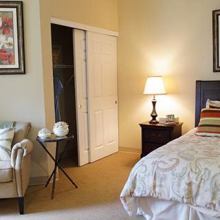 A cozy bedroom interior with a bed, nightstand, and armchair next to an open closet.