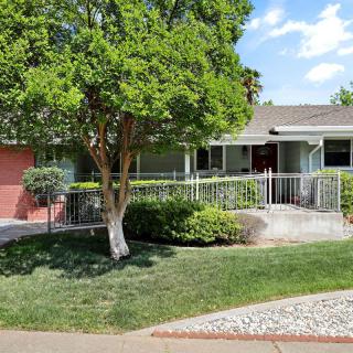 A suburban house with a front yard and a large tree, surrounded by a fence.