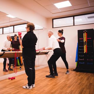 A group of people engaging in a fitness class with various equipment and mirrors in a gym setting.