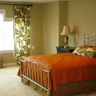 A cozy bedroom with an orange bedspread, leafy curtains, and a bedside lamp.