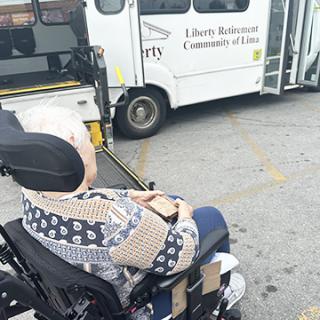 An elderly individual in a wheelchair awaits transportation from a community service.
