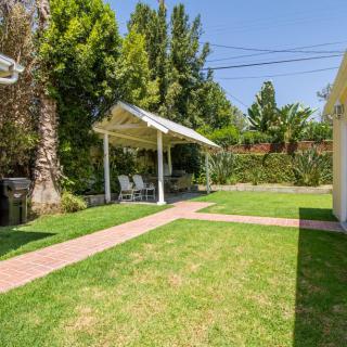 A well-maintained backyard with a lush lawn, shaded patio area, and vibrant trees.