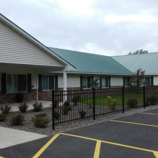 A building with a green roof and black fence, situated next to a parking lot under a cloudy sky.
