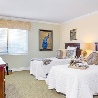 A cozy bedroom with twin beds, featuring elegant decor and a framed peacock artwork.