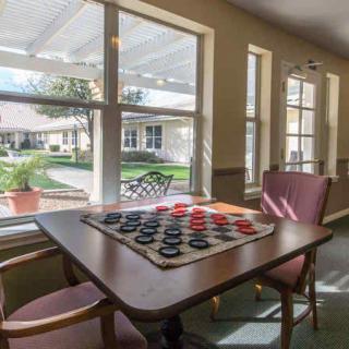 A cozy lounge area with a checkers board set up on a table, bathed in natural sunlight through large windows.