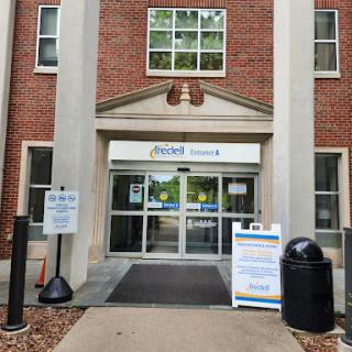 The entrance of a brick building featuring large glass doors and signage.