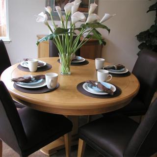 A round dining table set with place settings and a vase of flowers in the center.