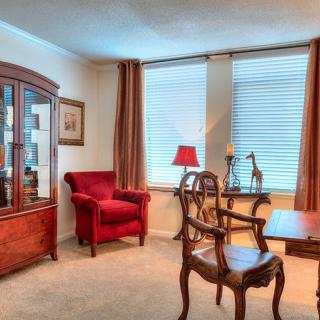 A cozy living room featuring classic wooden furniture, a red armchair, and large windows with curtains.